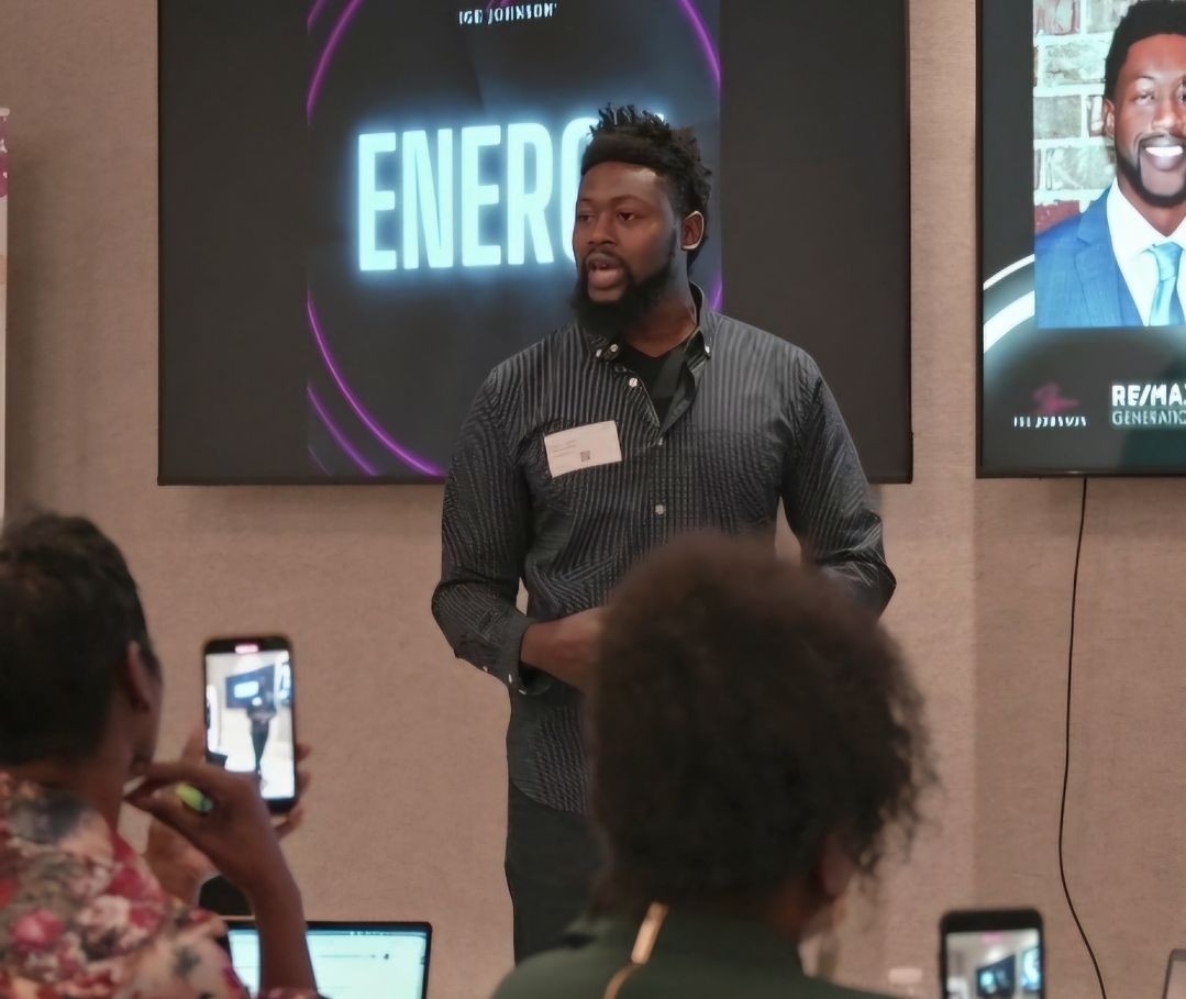 Man speaking in front of an audience at a presentation with energy-themed graphics on screen behind him.