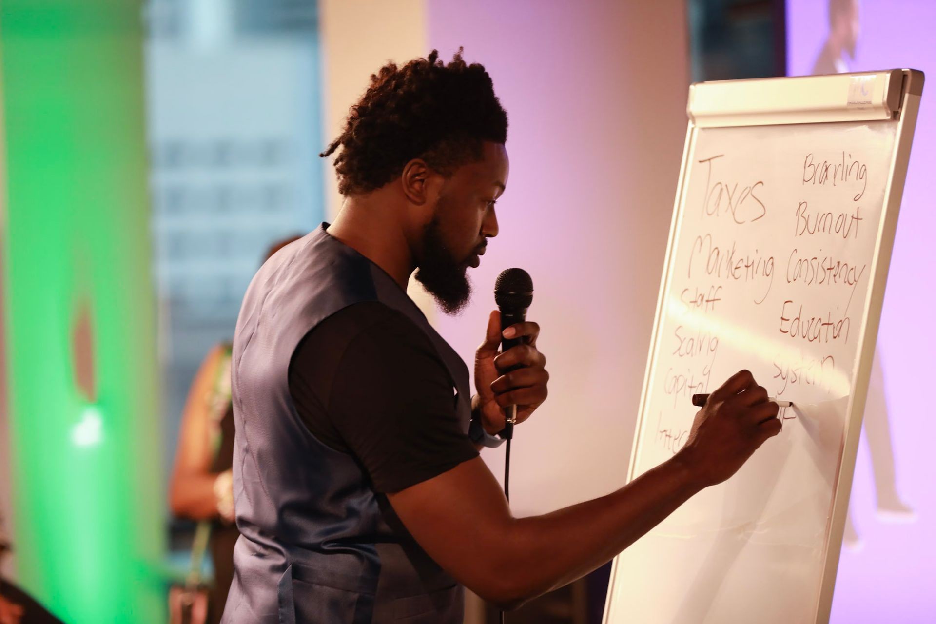 Man holding a microphone and writing on a whiteboard with various business-related keywords.